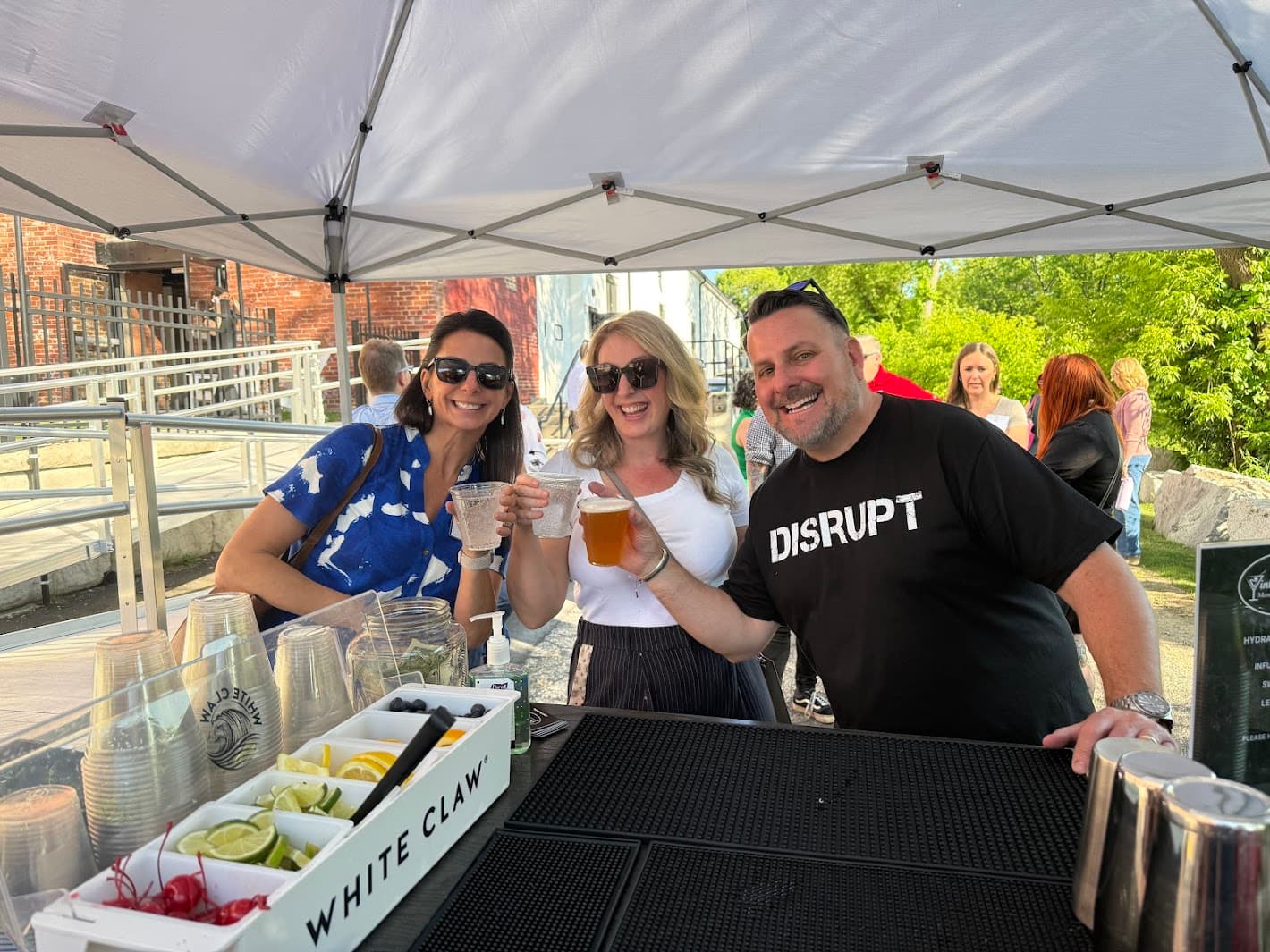 Three happy guests toasting and celebrating with drinks at outdoor event
