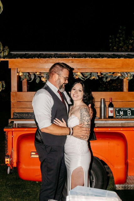 Bride and groom embracing in front of the 1968 Chevy tap trailer at reception