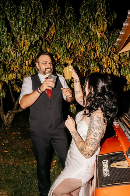 Couple toasting drinks from the 1968 Chevy tap trailer at nighttime wedding
